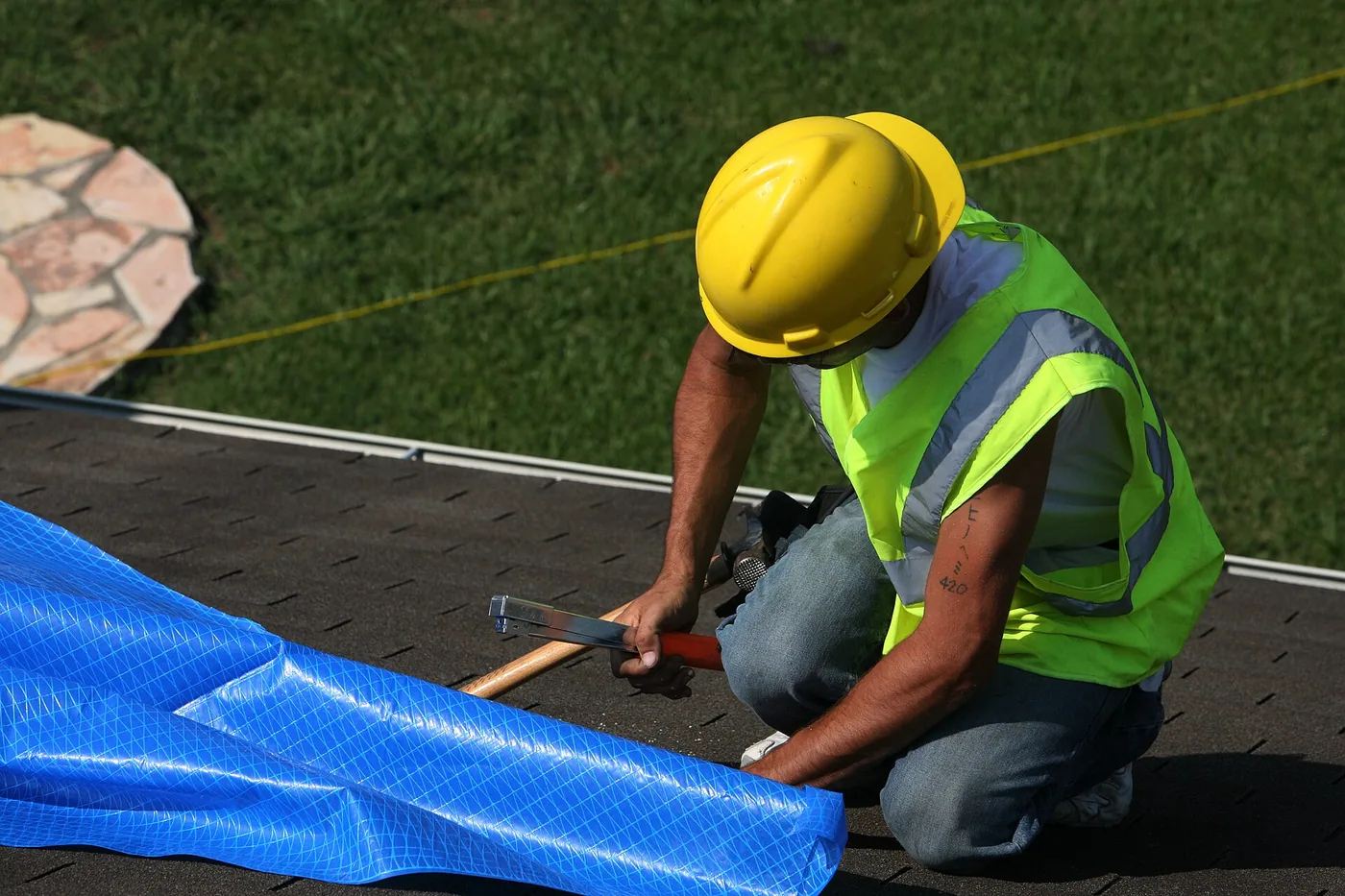 Roofer fastening a blue emergency roof tarp on a storm-damaged shingle roof — emergency roof tarping Pensacola FL